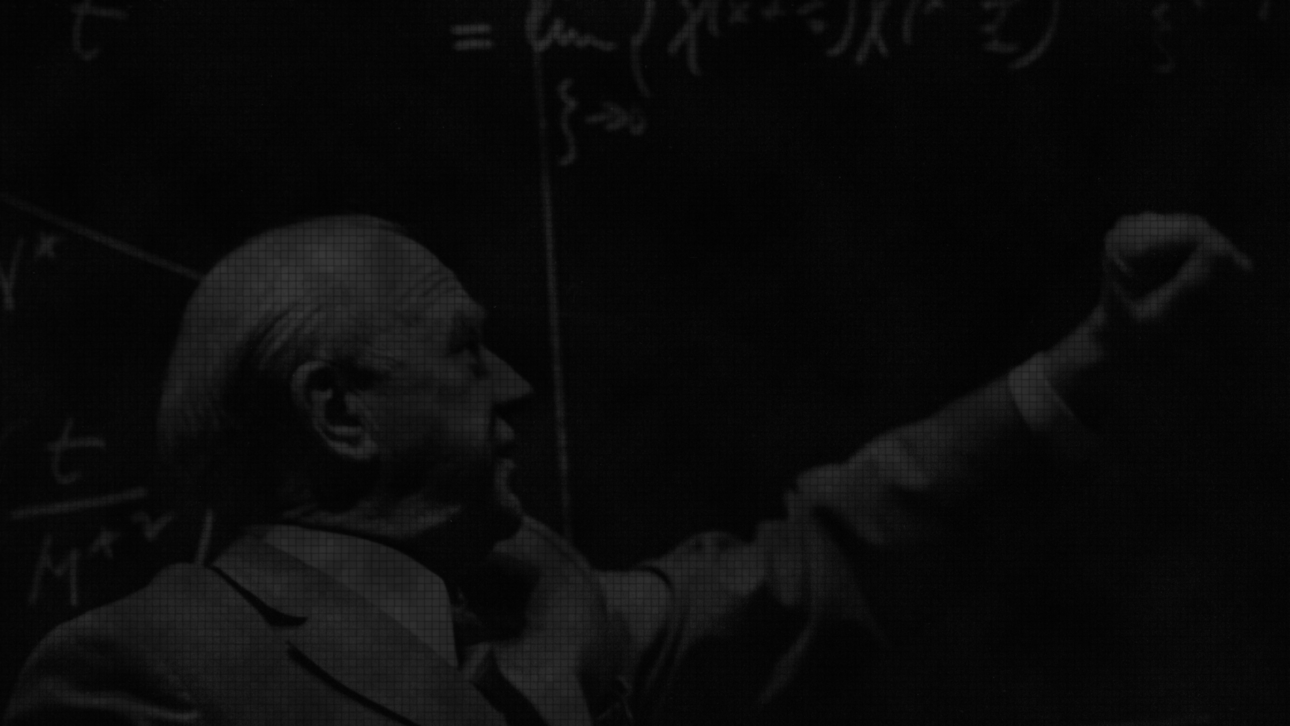 Werner Heisenberg lecturing in front of a blackboard with mathmatical equations.